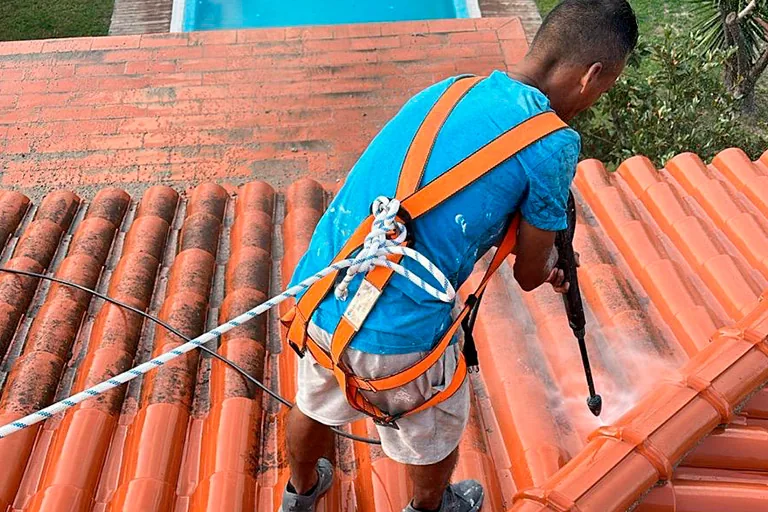 Operario con arnés de seguridad reparando un tejado de tejas