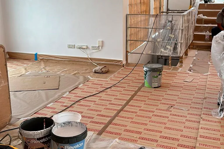 Salón protegido con plásticos y botes de pintura antes de pintar